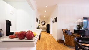 A modern kitchen with a wooden floor, white cabinetry, and a dining area with wicker furniture. - Beautiful apartment in a dream location near the Festival Hall (Baden Baden)