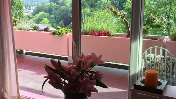 A room with a view of a balcony, a table with a vase of flowers, and a chair with a candle. - Beautiful apartment in a dream location near the Festival Hall (Baden Baden)