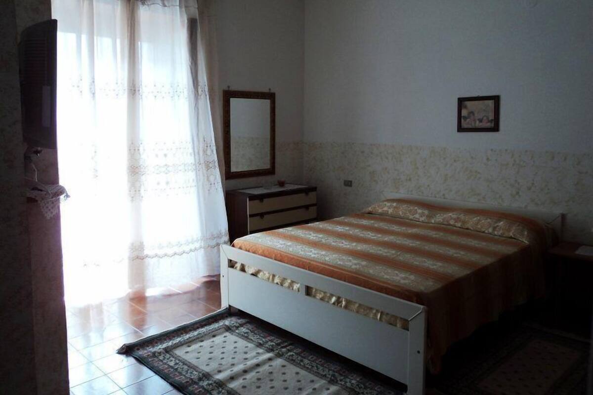 Une chambre à coucher avec un lit, une commode, un miroir et une fenêtre avec des rideaux.