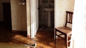Ein Zimmer mit einem Bett, einem Sessel, einem Fernseher, einem Badezimmer mit Waschbecken und Spiegel sowie einem gefliesten Boden.