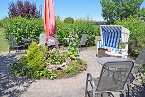 Ein Terrassenbereich im Freien mit Sitzgelegenheiten, einem roten Sonnenschirm und einem Garten mit verschiedenen Pflanzen.