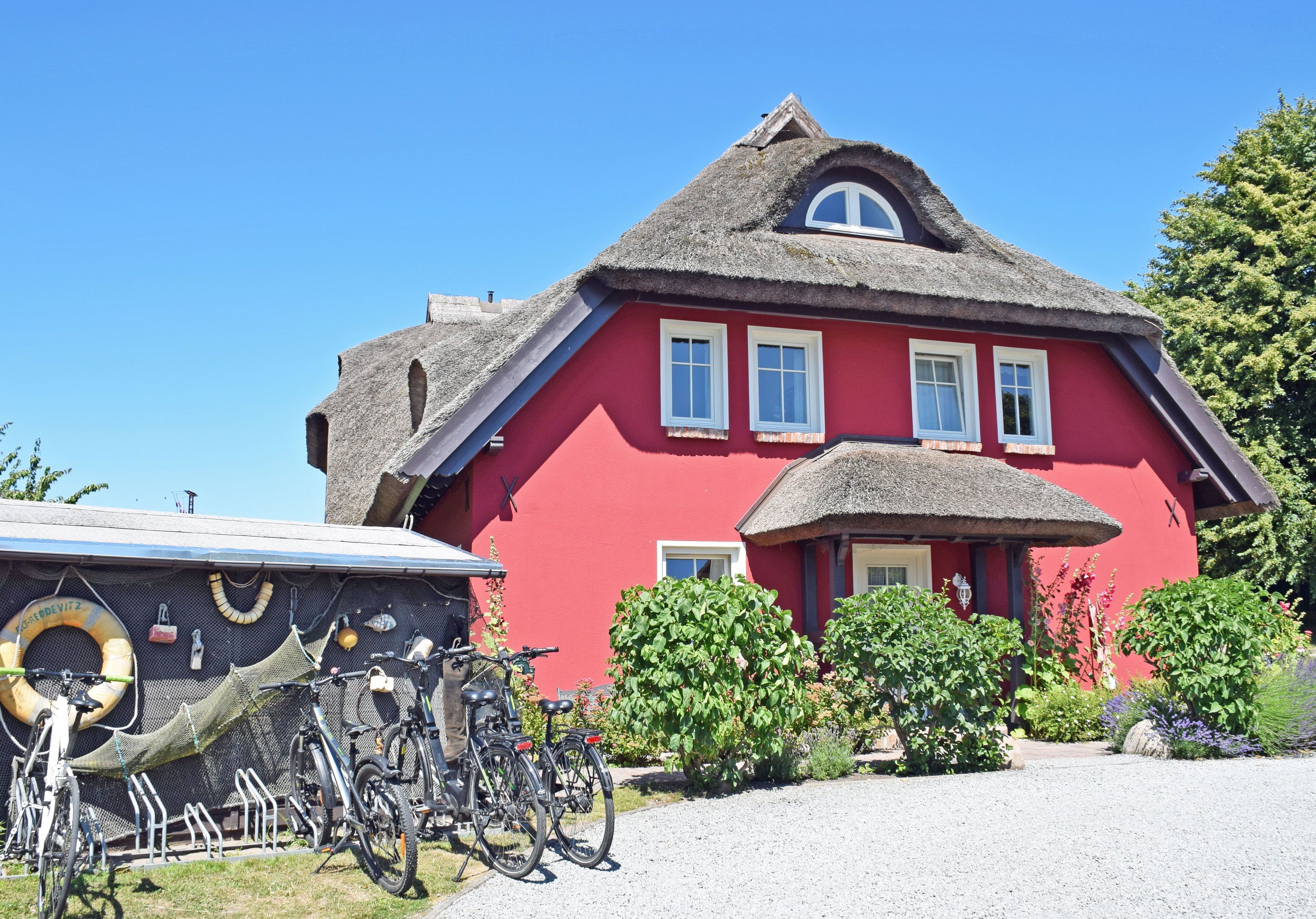 Een rood gebouw met rieten dak, fietsen en een grindpad.