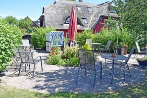 Eine Terrasse mit Gartenmöbeln, einem roten Sonnenschirm und einem Gebäude mit Strohdach im Hintergrund.