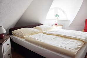 Une chambre à coucher avec un lit, une table de chevet, une lampe et une fenêtre agrémentée d’une plante.