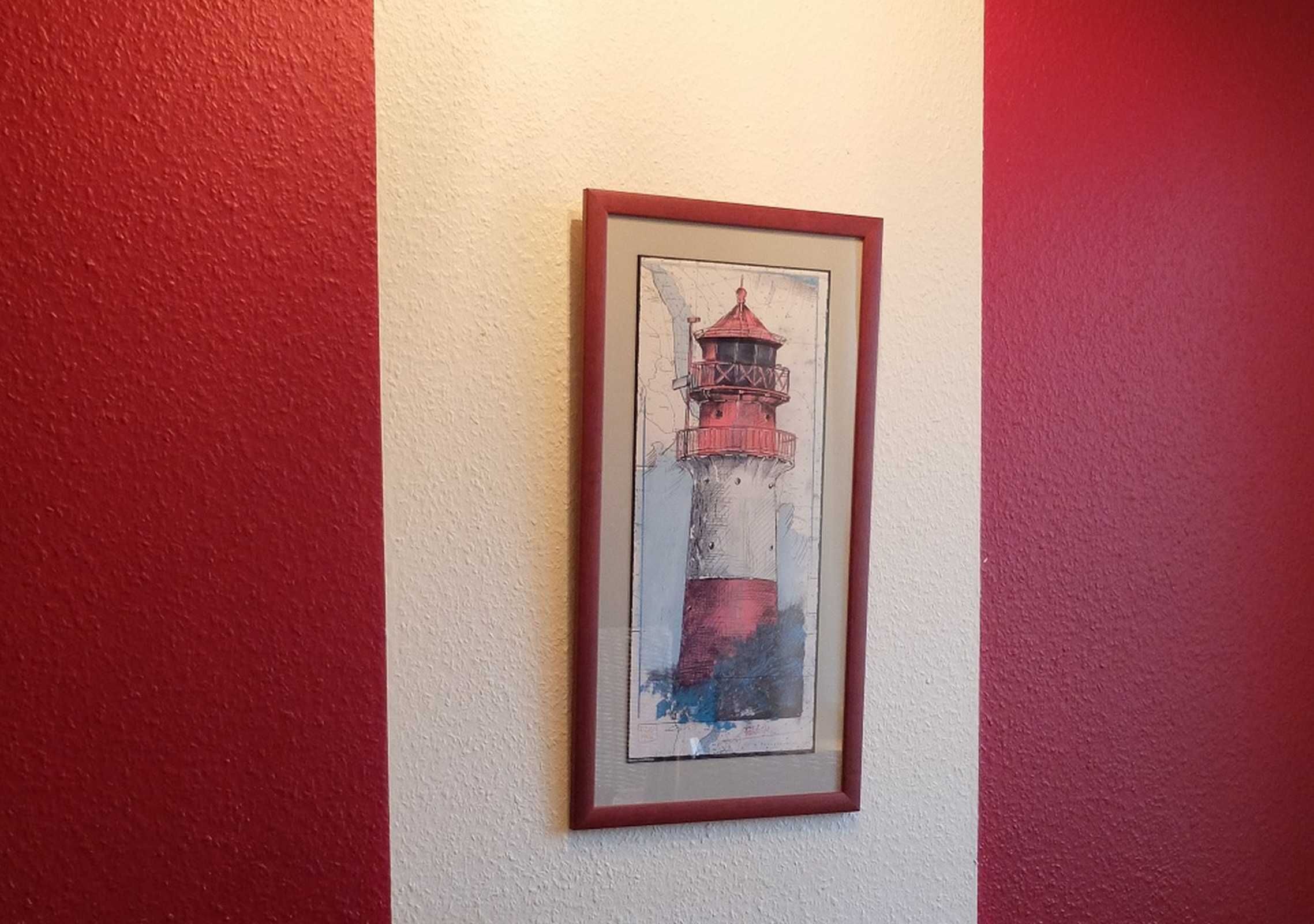 Een ingelijst kunstwerk van een vuurtoren op een muur.