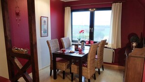 Un comedor con una mesa preparada para cuatro personas, sillas de mimbre y vistas a través de un ventanal.