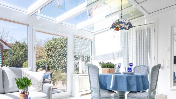 A bright sunroom with a table and chairs, large windows, and a hanging light fixture.