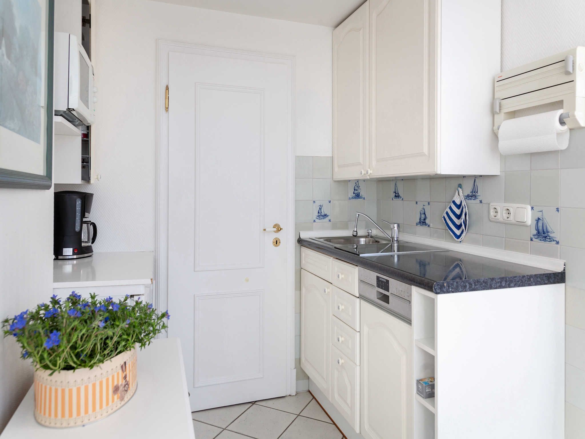 A kitchen with white cabinets, a black countertop, a coffee maker, a sink, and a potted plant with blue flowers.