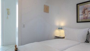 A neatly made bed with white linens, a bedside lamp, and a framed picture on the wall.