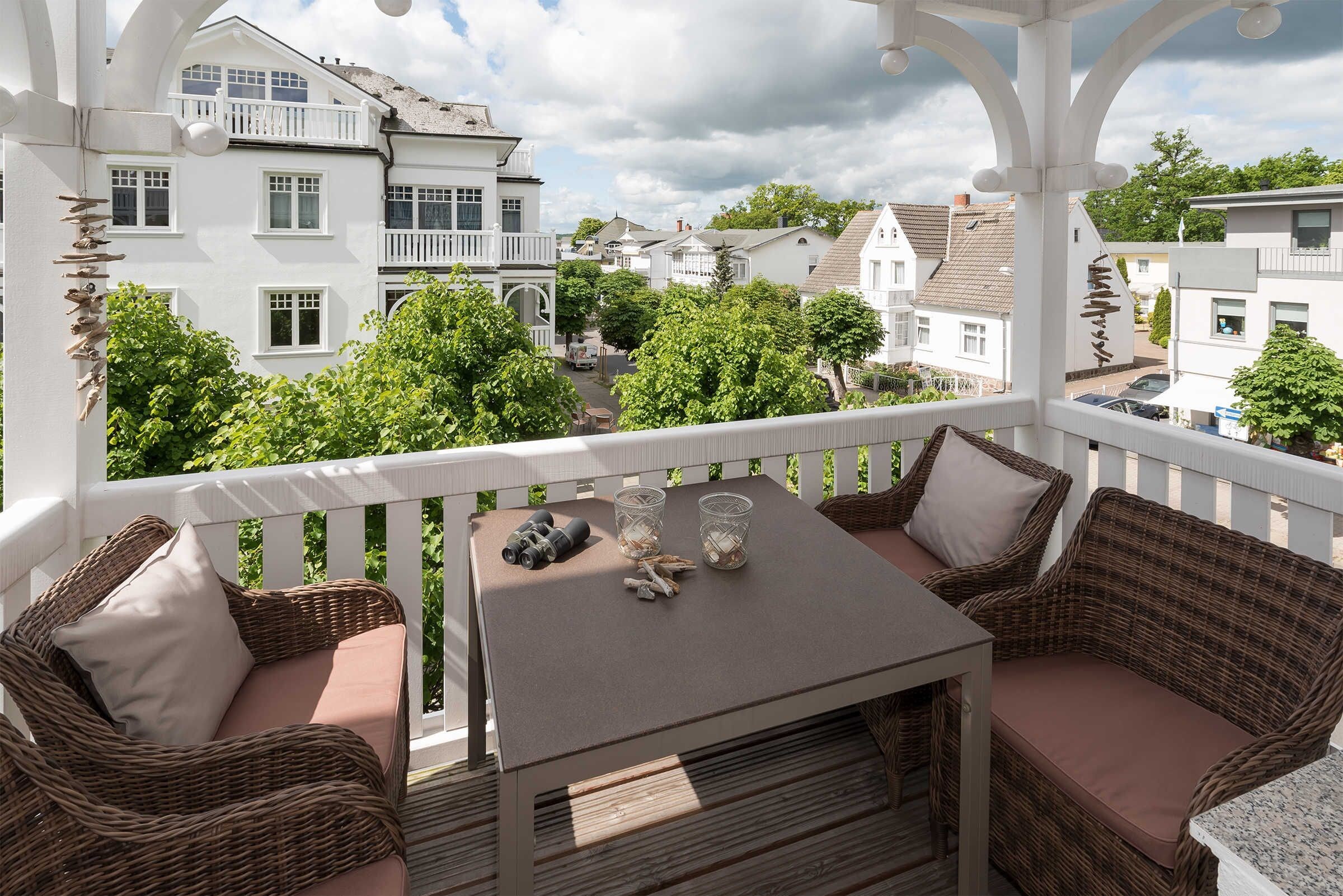 A balcony with wicker furniture, a table, and a view of surrounding buildings.