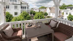 Een balkon met rieten meubilair, een tafel en uitzicht op omliggende gebouwen.
