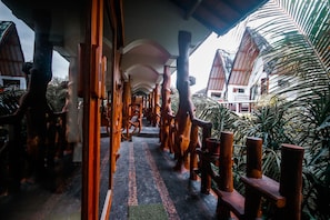 A corridor with wooden railings and a tiled floor, leading to a building with a sloped roof. - Sayang Mama Inn (Gili Air)