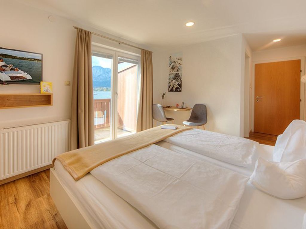 A hotel room with a bed, a desk, a chair, a window with a view, and a door.