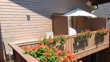 A wooden deck with a wooden railing, a white umbrella, and red flowers.