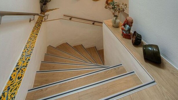 Eine Holztreppe mit Metallgeländer, eine Wand mit dekorativen Hüten und ein kleiner Tisch mit Vase und Figur.