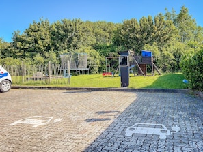 A paved area with a playground, a fence, and a vehicle.