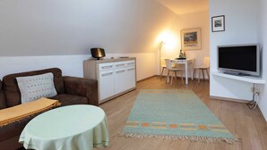Un salon avec un canapé marron, une petite table ronde, un meuble blanc, un téléviseur et un tableau accroché au mur.