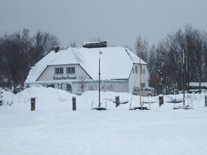 Een gebouw met de tekst 'Räucherlhaus', met een sneeuwbedekte dak, omringd door sneeuw en bomen.