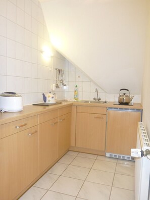 Een kleine keuken met een spoelbak, waterkoker, broodrooster en afdruiprek.