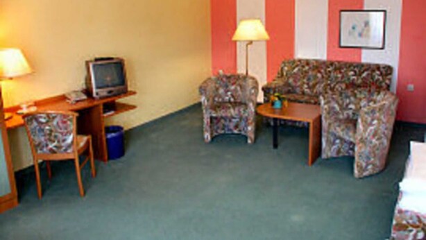 A hotel room with a desk, a television, a floral sofa, two armchairs, and a small table.