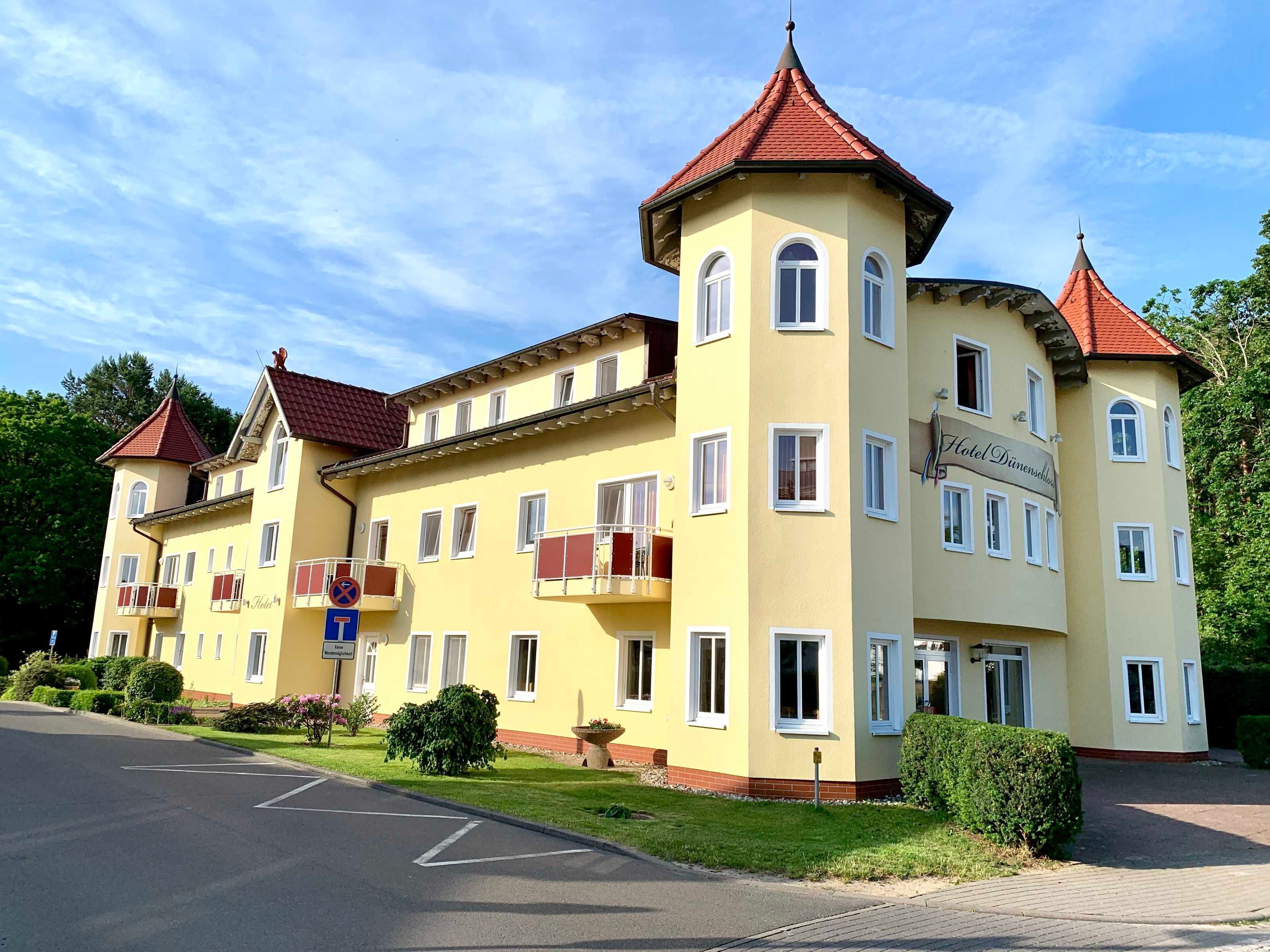 A yellow building with red roofs, multiple balconies, and a sign indicating a hotel.