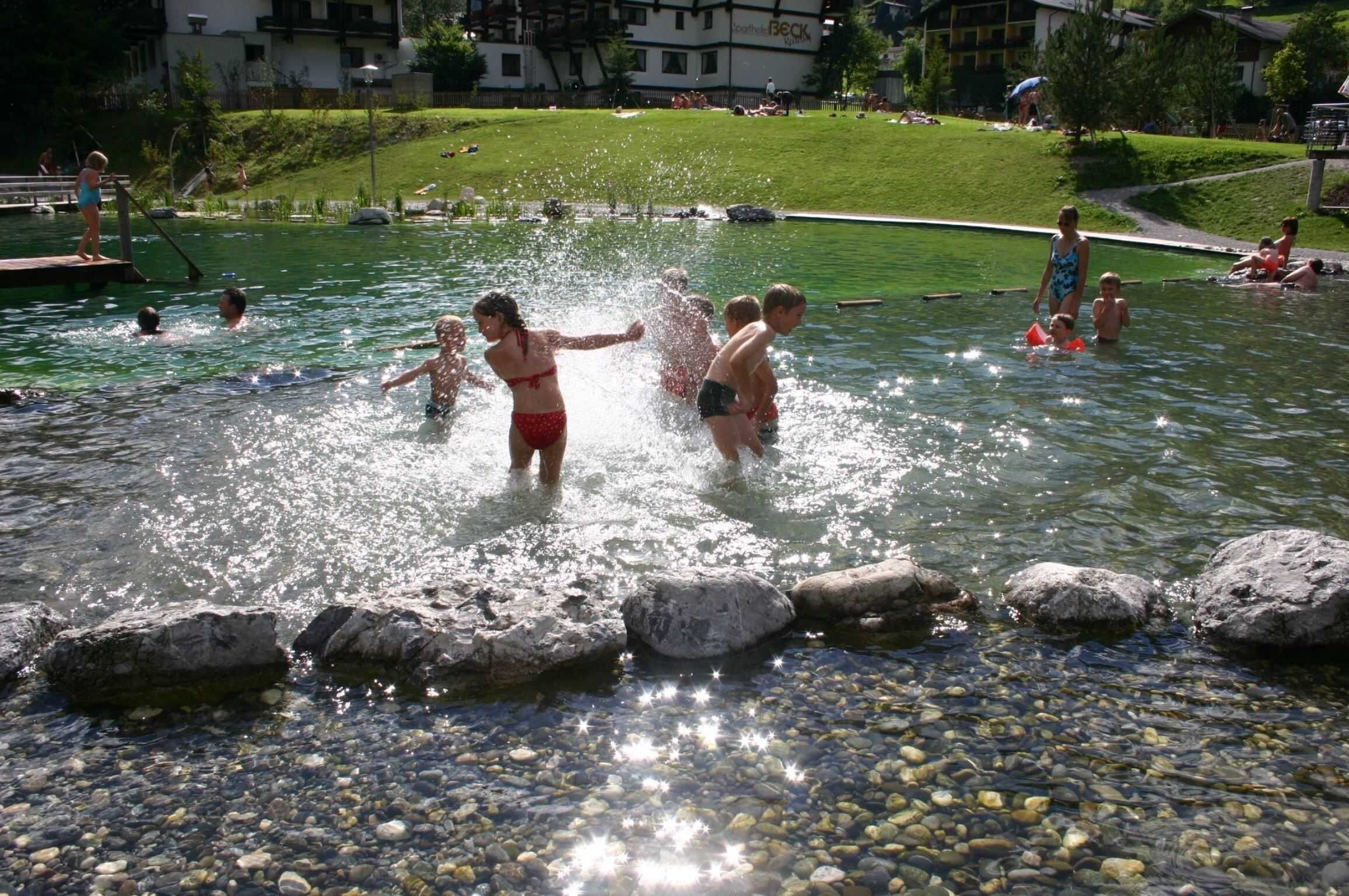 Una piscina con gente disfrutando en el agua, rodeada de rocas y piedras.