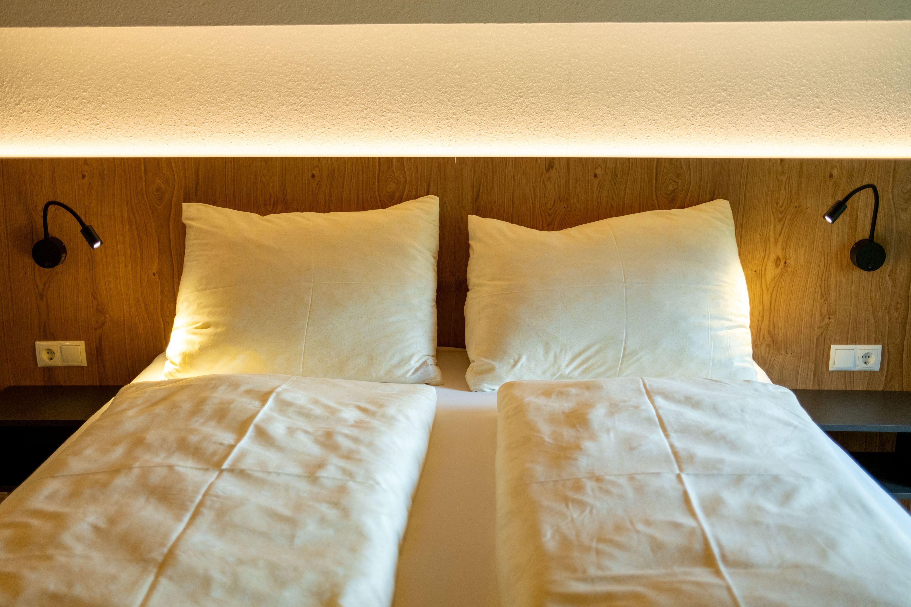 A double bed with white linens, two bedside lamps, and a wooden headboard.