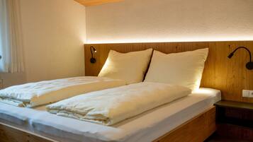 Un letto matrimoniale con due cuscini, una testiera in legno e un comodino con una lampada.