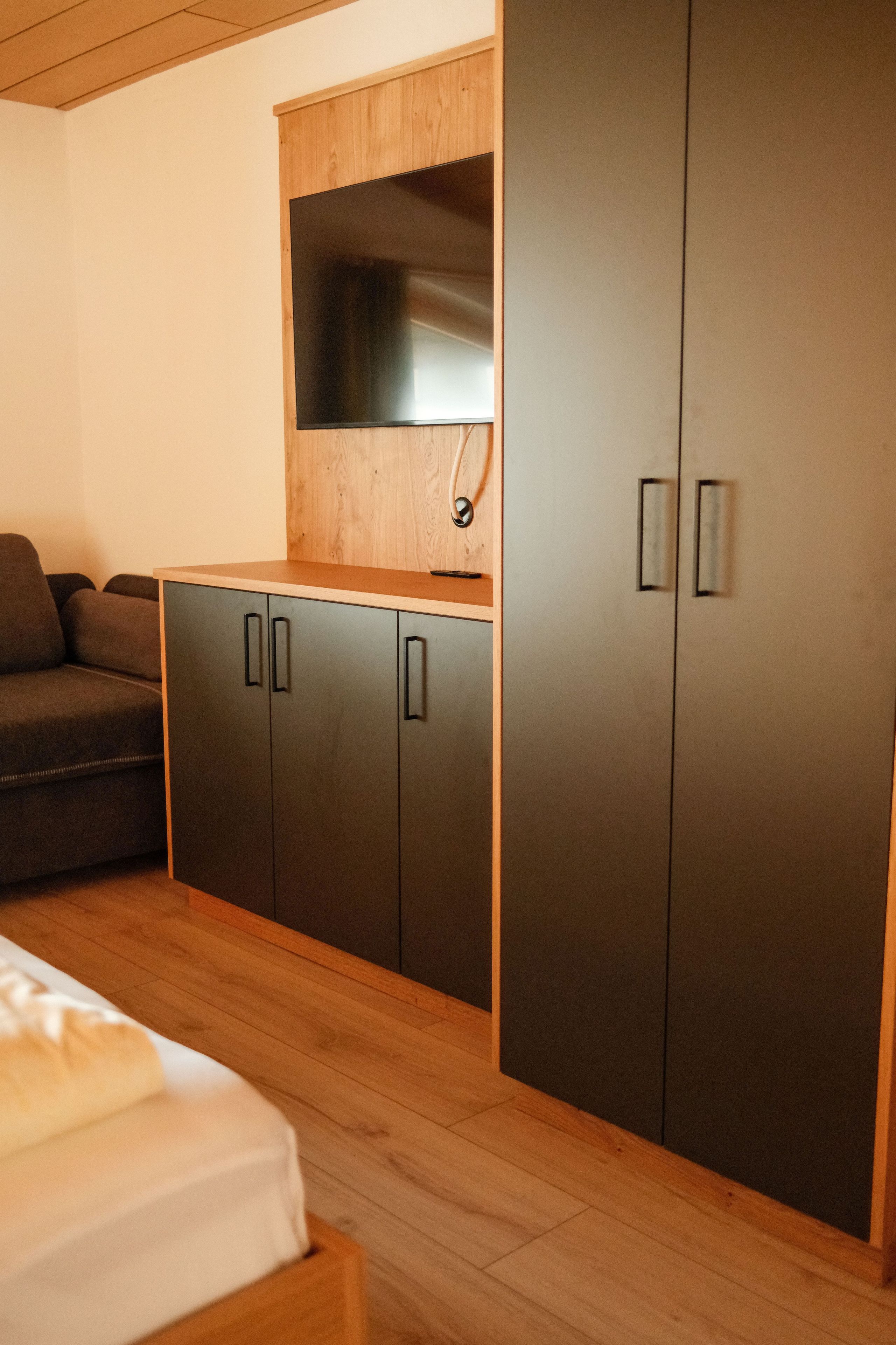 Un dormitorio con una cama, un aparador de madera, un armario oscuro y un televisor de pantalla plana montado en la pared.