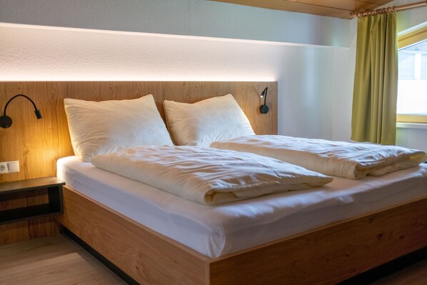 A neatly made bed with a wooden headboard, two bedside lamps, and a window with curtains.