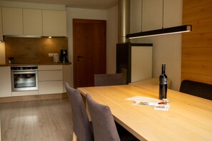 A modern kitchen with a built-in oven, a coffee machine, and a wooden dining table with chairs.