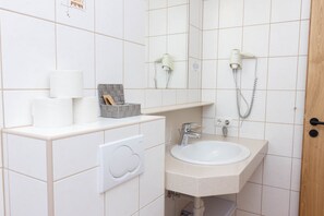 Une salle de bain avec un lavabo blanc, un miroir, un sèche-cheveux et un porte-rouleau de papier toilette.