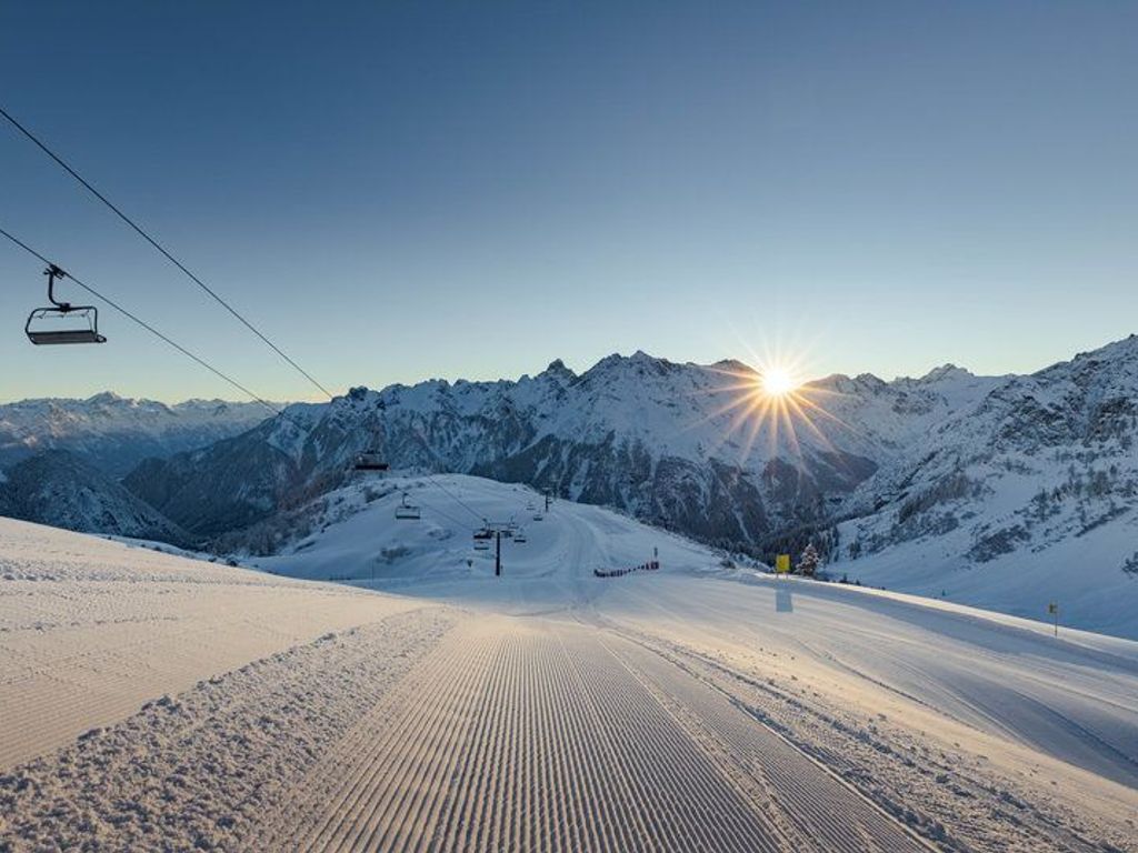 A snow-covered ski slope with a ski lift and mountains in the background.