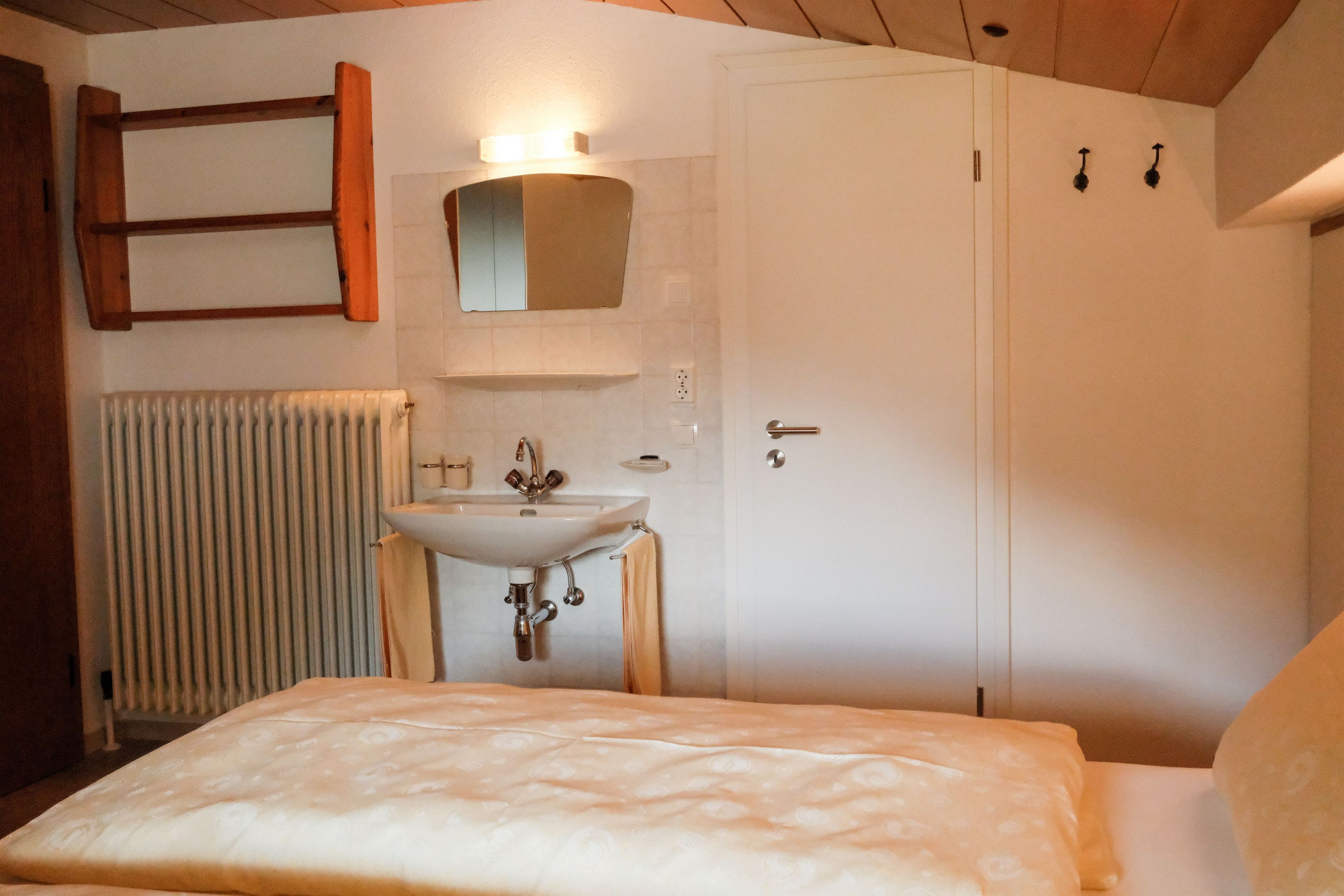 Un dormitorio con una cama, una mesita de noche, un lavamanos blanco instalado en la pared, un espejo y un radiador.