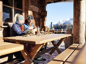 A wooden cabin with a table set for two, a mountain view, and a snowy landscape.