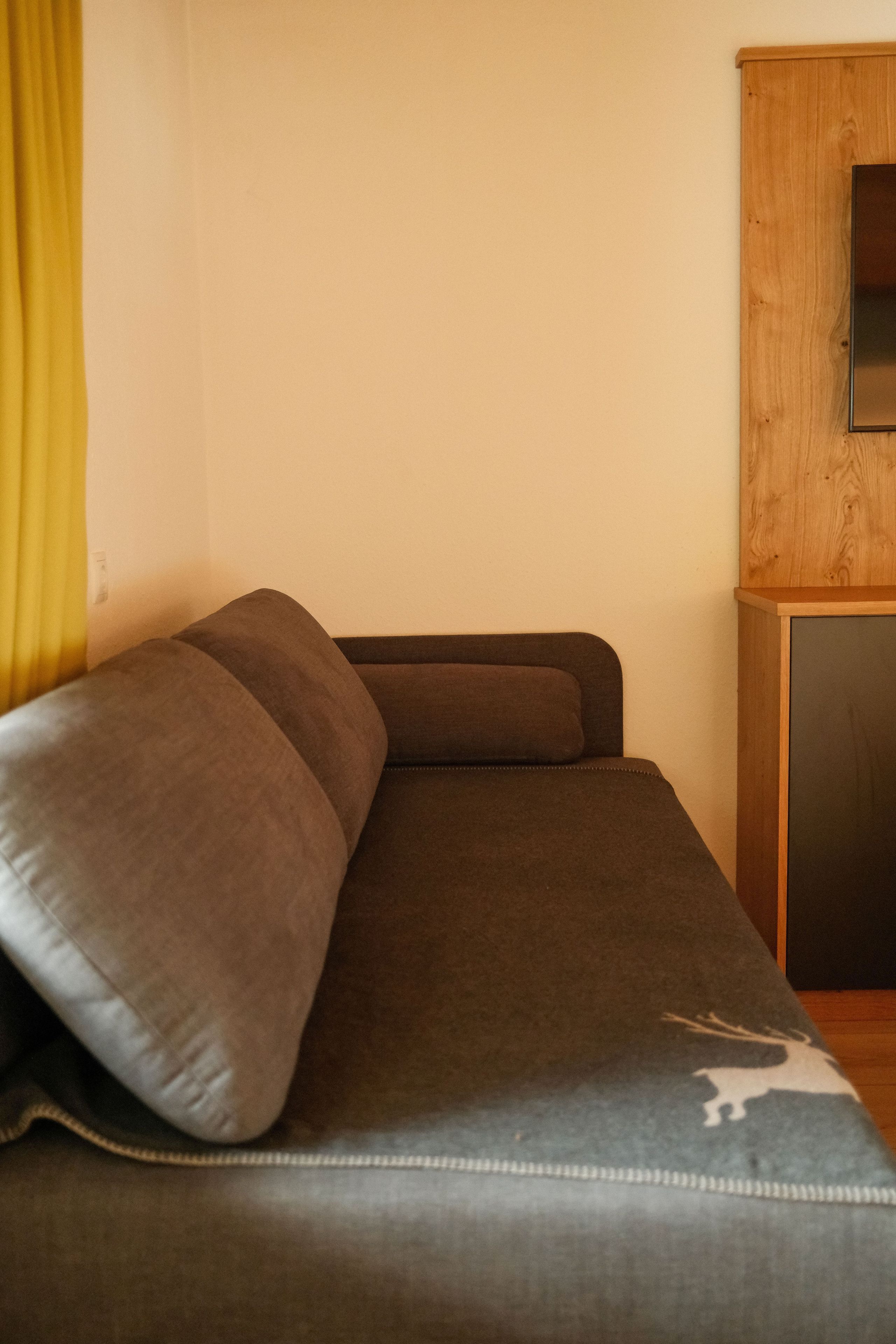 Un lit simple avec une tête de lit, une table de chevet en bois et un rideau jaune.