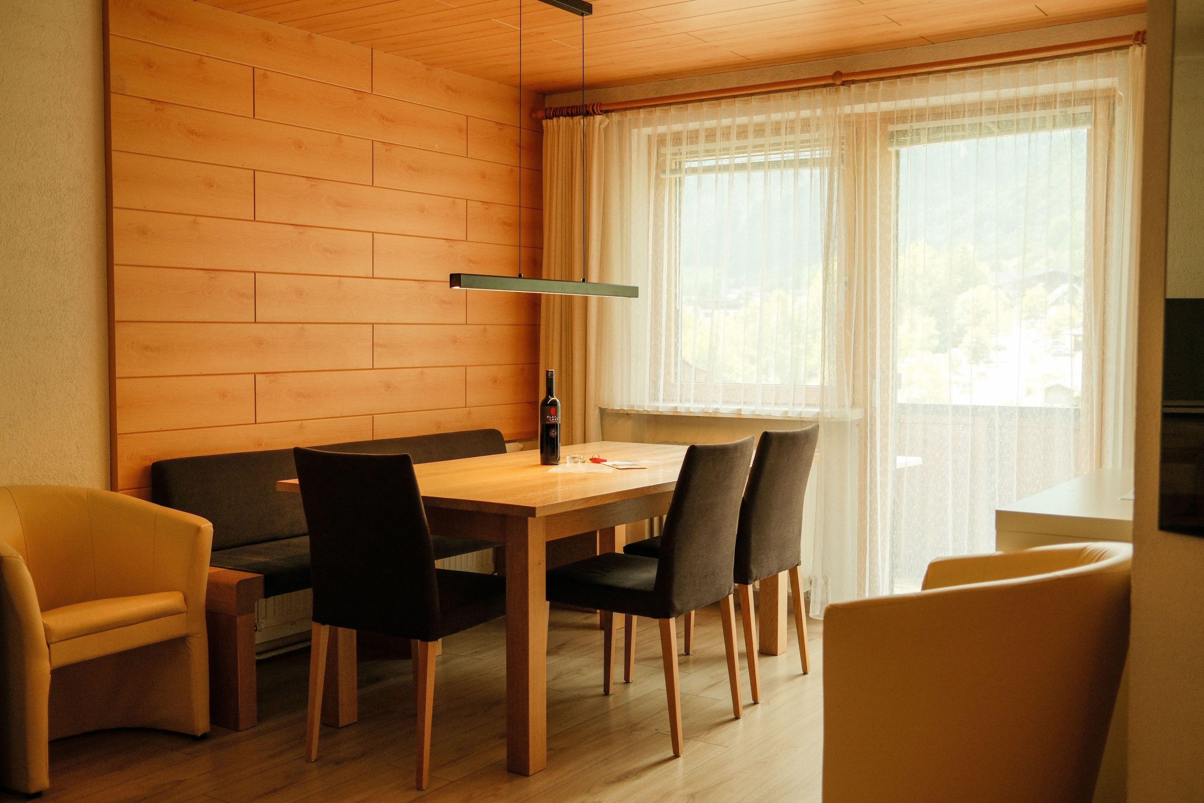 A dining area with a wooden table and chairs, a sofa, and a window with sheer curtains.