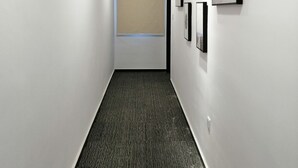 Un pasillo con piso alfombrado, paredes blancas y luces en el techo.