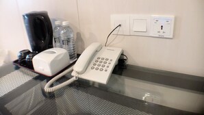 Habitación de hotel con una mesa de vidrio, un teléfono blanco, dos botellas de agua y una cafetera negra.