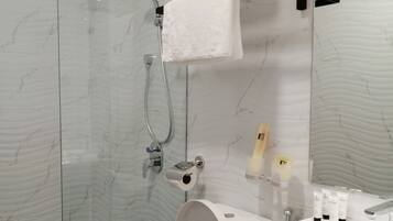 Moderni kylpyhuone, jossa on lasiseinällä varustettu suihku, valkoinen wc-istuin ja pesuallas, jonka päällä on hygieniatuotteita.