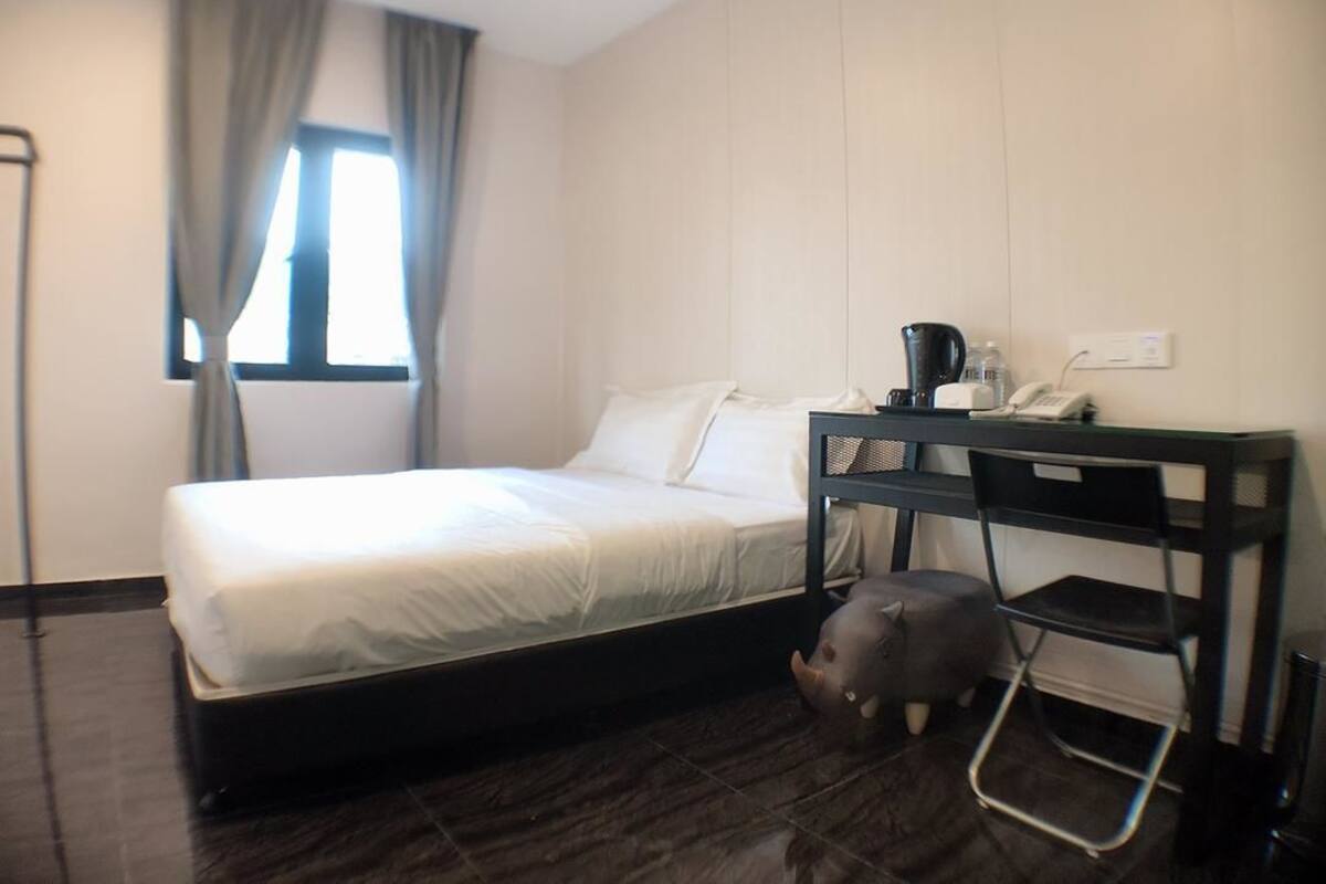 A hotel room with a bed, a desk with a telephone, a coffee maker, and a small elephant figurine.