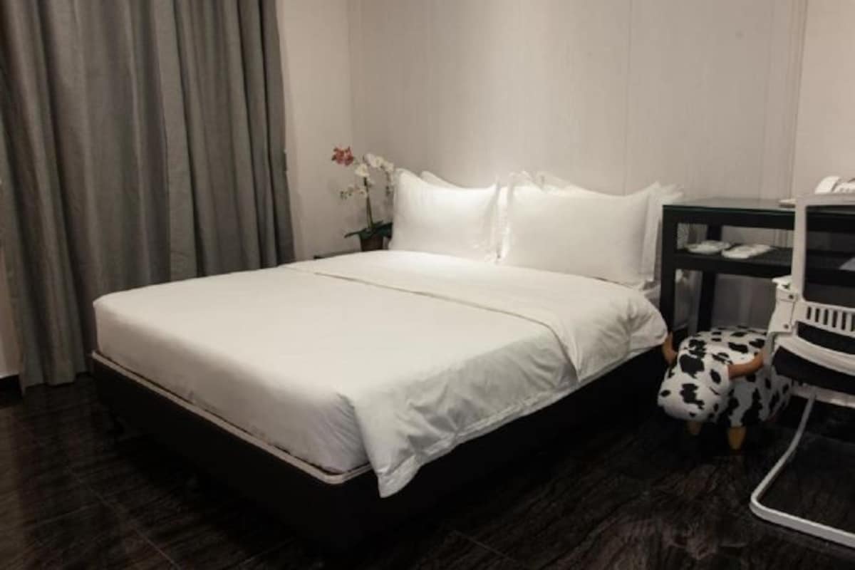 Habitación de hotel con una cama grande, una mesita de noche, una silla y una pequeña mesa con un teléfono.