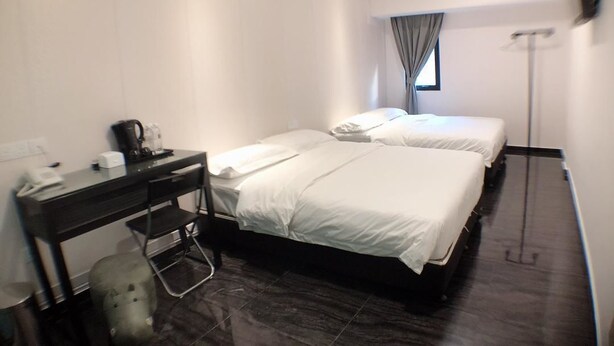 Habitación de hotel con dos camas, un escritorio con teléfono y cafetera, un cesto de basura y una lámpara de pie.