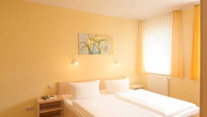 A hotel room with two beds, a nightstand, a painting on the wall, and a window with curtains. - Vacation apartment WE18 - Holiday apartments at the sports field (Sellin)