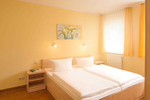 A hotel room with two beds, a nightstand, a painting on the wall, and a window with curtains.