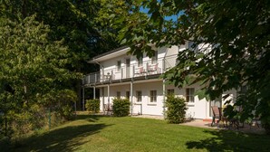 A two-story building with a balcony, surrounded by greenery and trees. - Vacation apartment WE18 - Holiday apartments at the sports field (Sellin)