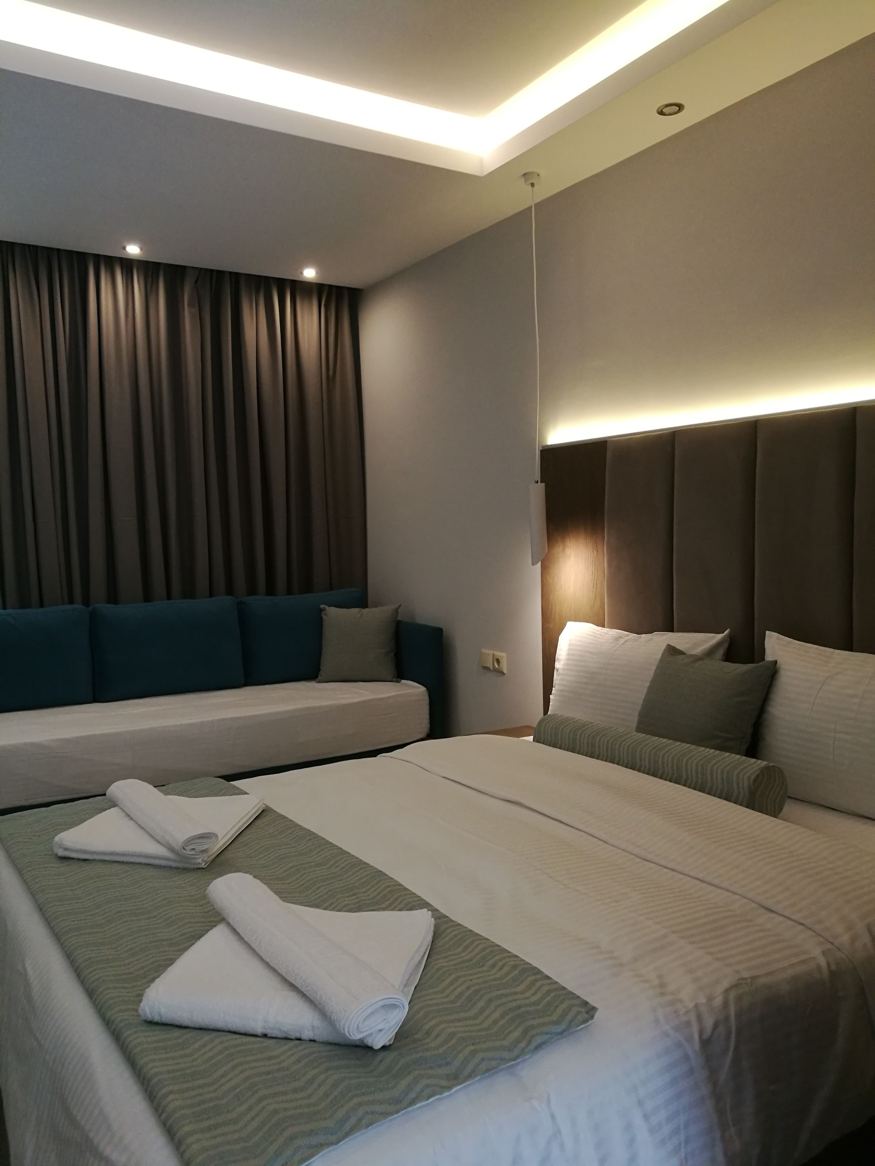 Ett hotellrum med två sängar, en soffa och ett stort fönster med gardiner.