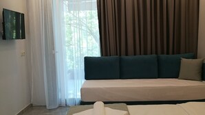 A modern hotel room with a large bed, a sofa bed, and a view of trees through sheer curtains. - 4-You Family 2 (Polygyros)