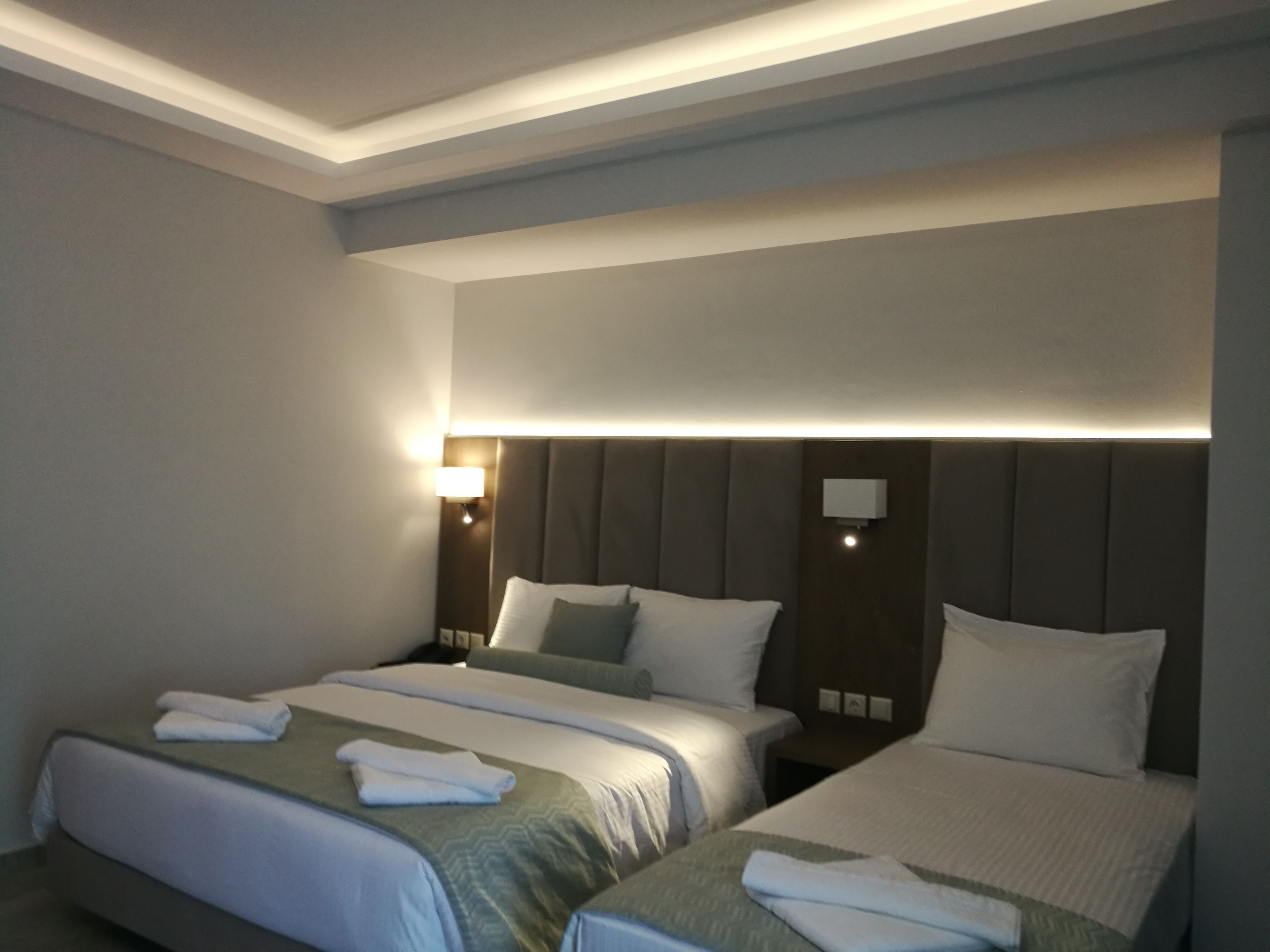 A hotel room with two beds, each with a headboard, bedside tables, and lamps.