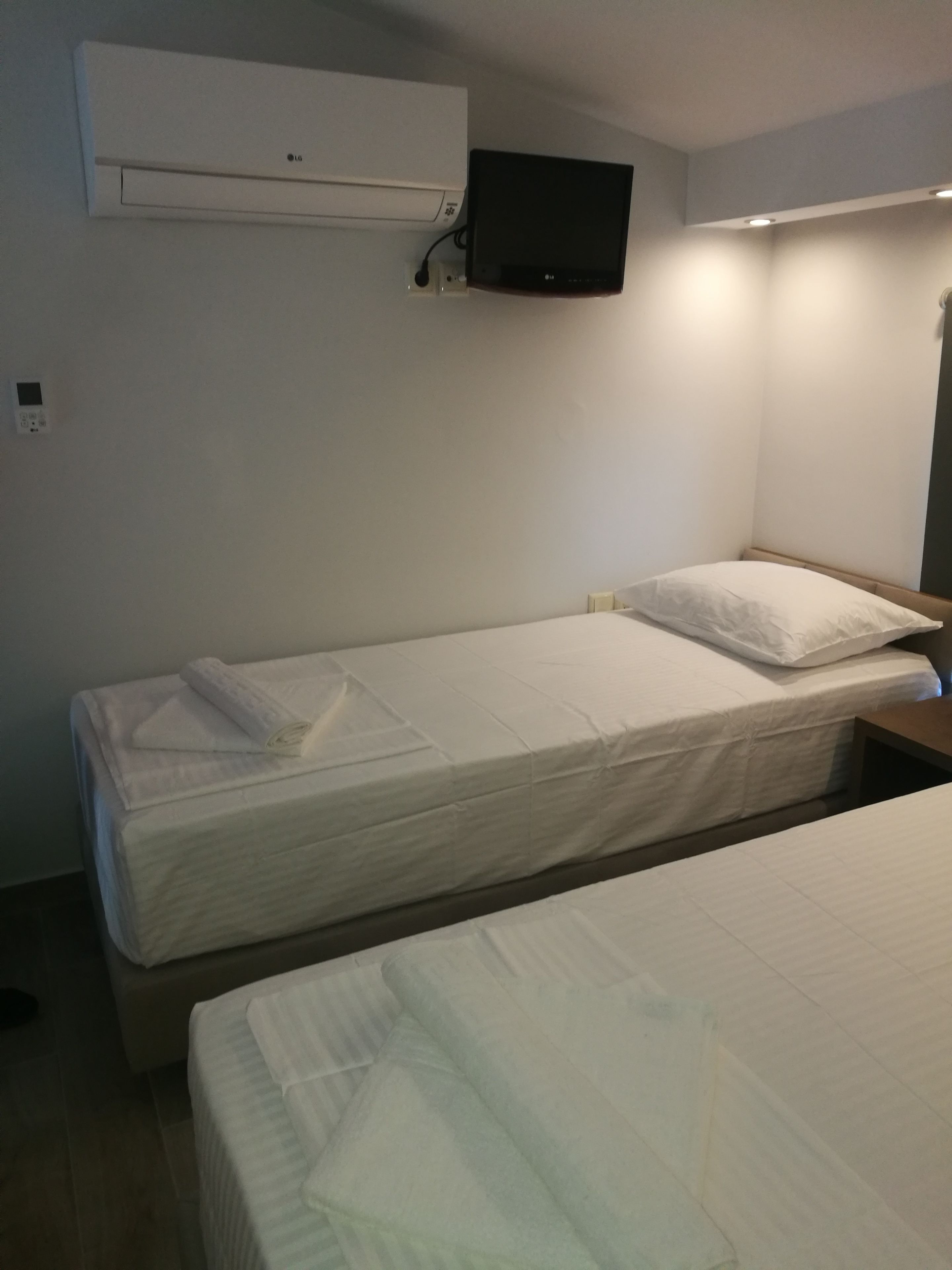 A hotel room with two beds, a flat-screen TV mounted on the wall, and a wall-mounted air conditioning unit.